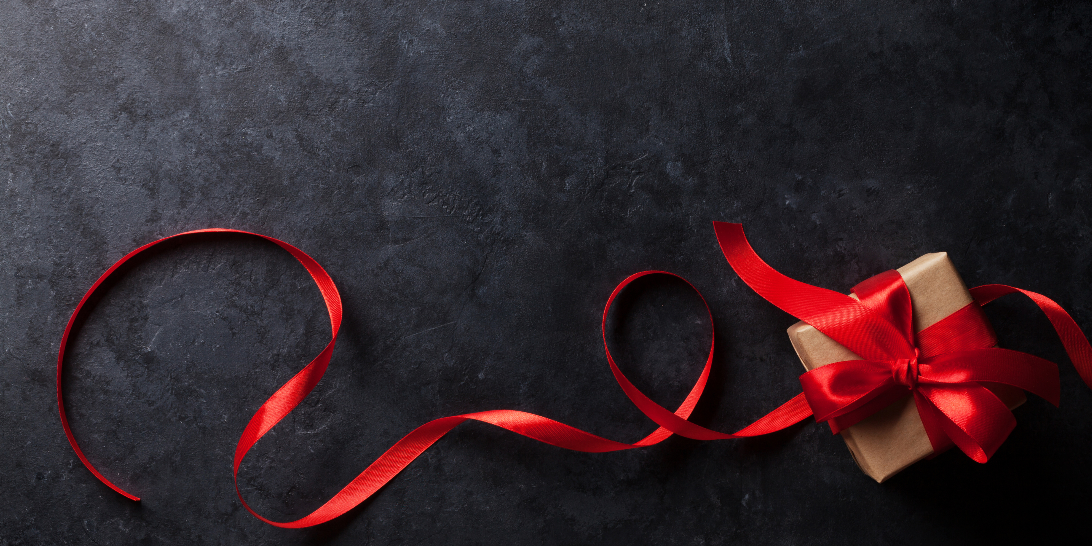 A black background with a brown paper wrapped box with red silk ribbon. 